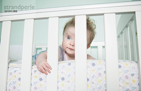 Porträt eines Mädchens  das durch Gitterstäbe auf dem Kinderbett schaut.
