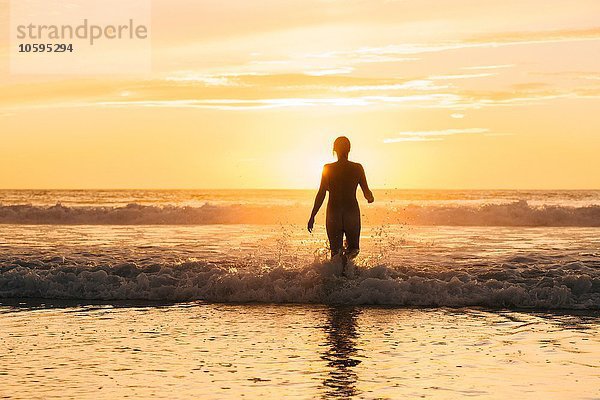 Rückansicht der Silhouette von nackten Frauen  die bei Sonnenuntergang in den Ozean gehen.