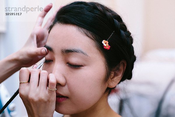 Hände des Maskenbildners beim Auftragen von Make-up auf eine junge Frau mit geschlossenen Augen