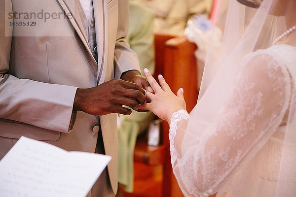 Beschnittene Ansicht des Bräutigams  der bei der Trauungszeremonie den Ring auf den Finger der Braut legt.