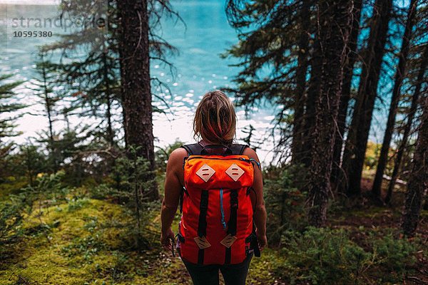 Hochwinkel-Rückansicht einer erwachsenen Frau mit orangefarbenem Rucksack im Wald mit Blick auf das Wasser  Moraine Lake  Banff National Park  Alberta Canada