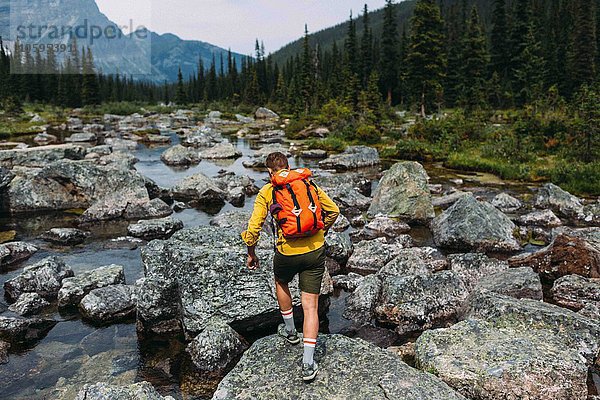 Rückansicht eines erwachsenen Mannes mit Rucksack auf felsigem Flussbett  Moraine Lake  Banff National Park  Alberta Canada