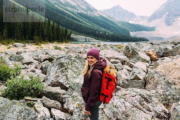Seitenansicht einer erwachsenen Frau auf einer felsigen Landschaft mit Rucksack und Blick auf die lächelnde Kamera  Moraine Lake  Banff National Park  Alberta Canada