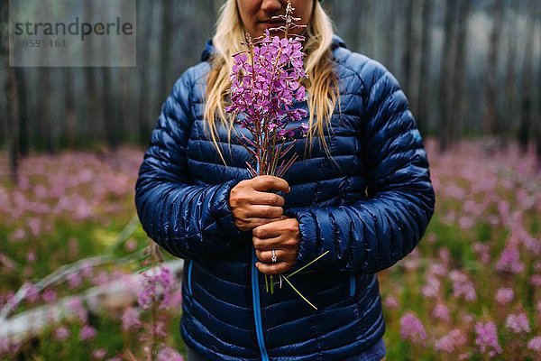 Ausschnitt einer erwachsenen Frau im gepolsterten Mantel mit Wildblumen  Moränensee  Banff National Park  Alberta Canada