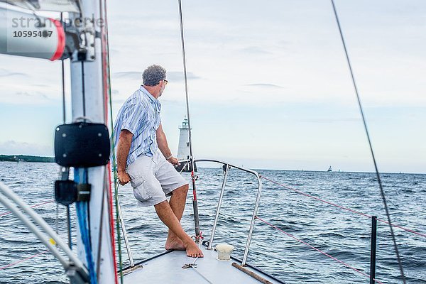 Erwachsener Mann am Bug eines Segelbootes mit Blick auf den Leuchtturm