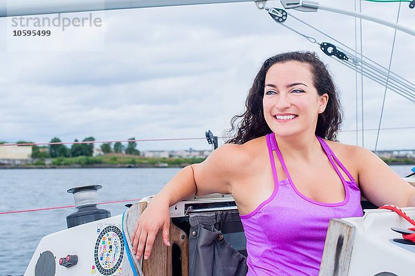Junge Frau mit Weste auf dem Segelboot lächelnd wegblickend