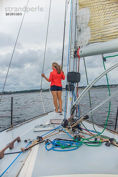 Durchgehende Rückansicht der jungen Frau auf dem Bug des Segelbootes mit Blick nach hinten
