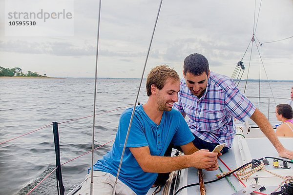 Männer auf dem Segelboot schauen lächelnd auf das Handy