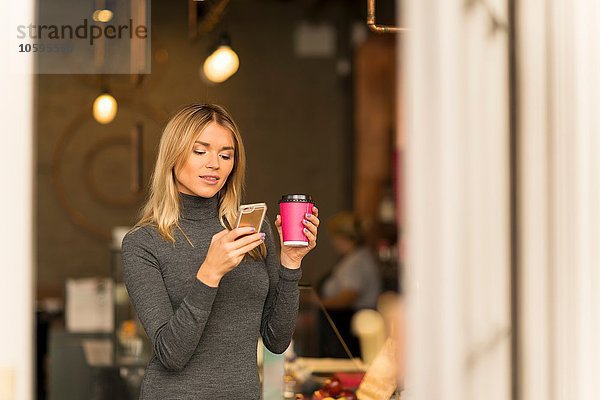 Frau mit Kaffee zum Mitnehmen per Smartphone