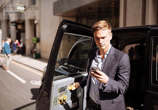 Geschäftsmann mit Smartphone beim Verlassen des schwarzen Taxis  London  UK