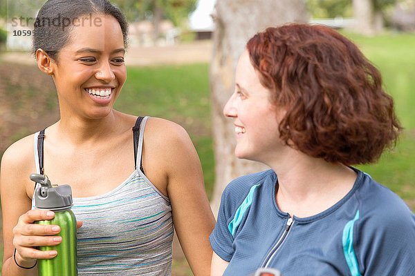Kopf und Schultern junger Frauen mit Wasserflaschen von Angesicht zu Angesicht lächelnd