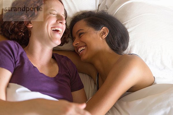 Hochwinkelansicht eines lesbischen Paares  das im Bett liegt und sich umarmt.