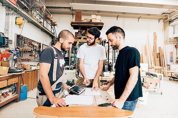 Freunde  die in der Schreinerei um die Werkbank herum stehen und sich unterhalten.