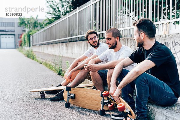 Seitenansicht der jungen Männer auf dem Bordstein mit Skateboards