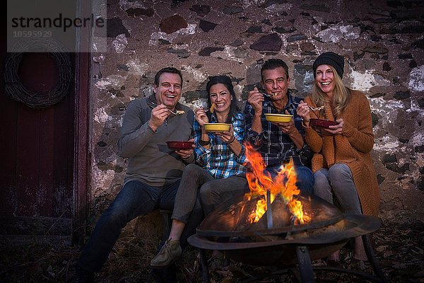 Porträt von zwei reifen Paaren  die nachts vor dem Lagerfeuer speisen.