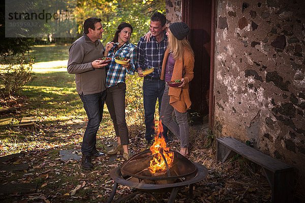 Zwei reife Paare beim Essen vor dem Lagerfeuer im Garten