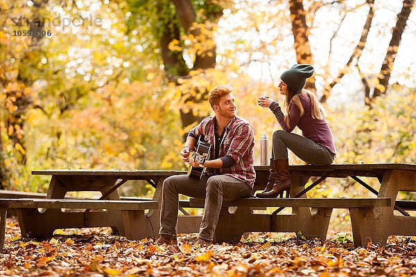Junges Paar spielt Gitarre auf Picknickbänken im Herbstwald