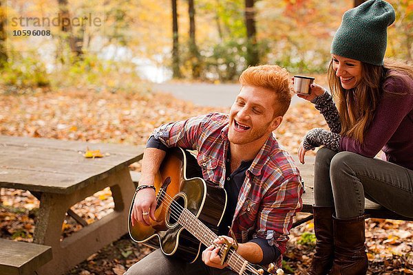 Junges Paar spielt Gitarre auf der Picknickbank im Herbstwald