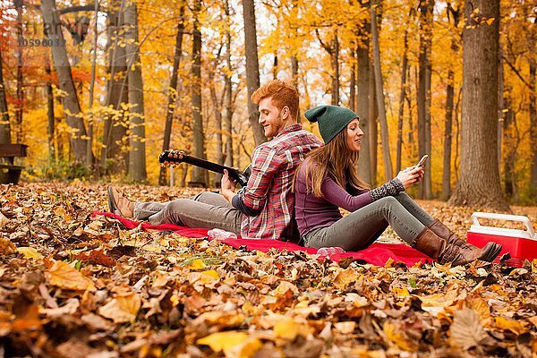 Junges Paar Rücken an Rücken auf Picknickdecke im Herbstwald