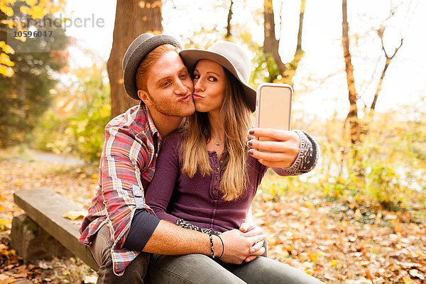 Junges Paar auf der Bank mit Smartphone Selfie im Herbstwald
