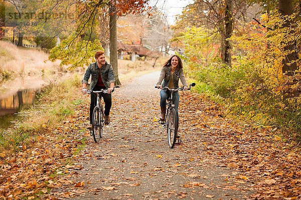 Glückliches junges Paar beim Radfahren am Flussufer im Herbst