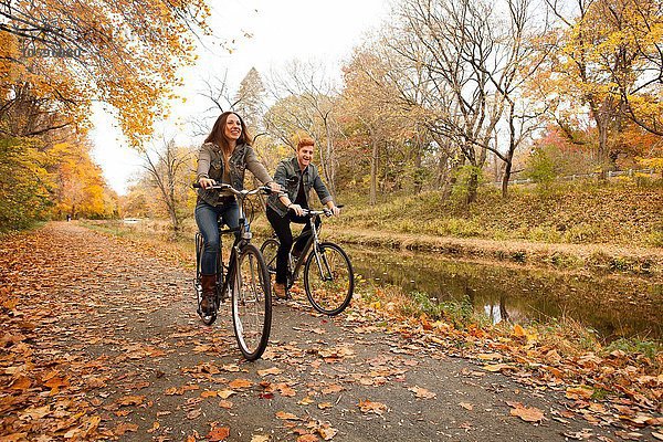Glückliches junges Paar  das im Herbst am Flussufer entlang radelt