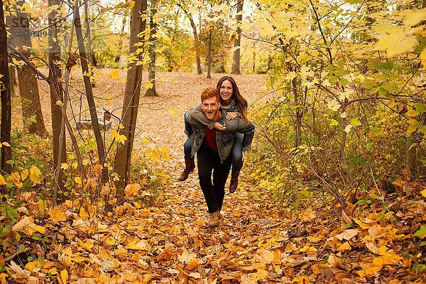 Romantischer junger Mann gibt Freundin ein Huckepack durch den Herbstwald