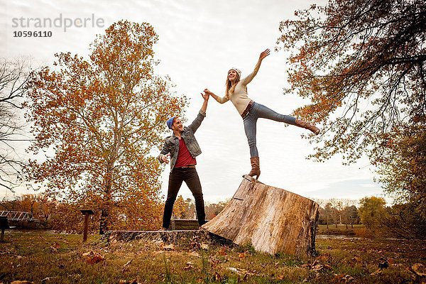 Junges Paar spielt auf Baumstumpf im Herbstpark