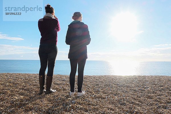 Rückansicht von zwei jungen erwachsenen Schwestern mit Blick auf das sonnige Meer