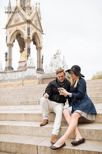 Junges Paar sitzt auf Stufen und liest Smartphone-Texte  Albert Memorial  London  England  UK