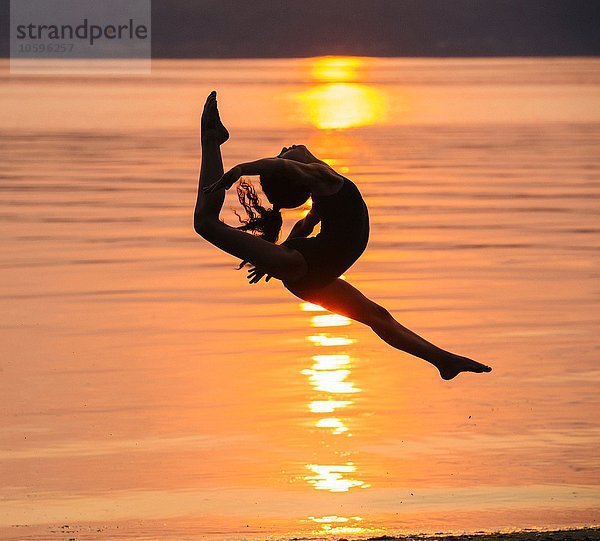 Seitenansicht des Mädchens in Silhouette am Meer bei Sonnenuntergang in der Luft  Beine auseinander  Kopf zurückwerfend