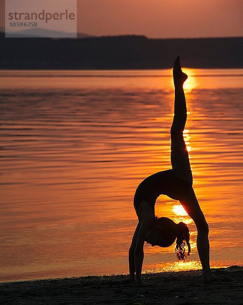 Seitenansicht des Mädchens in Silhouette am Meer bei Sonnenuntergang über das rückwärtige Bein gebeugt  das die Spalten macht