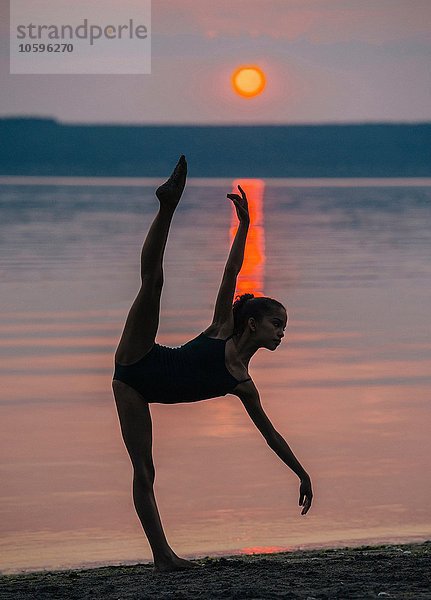 Mädchen am Meer bei Sonnenuntergang auf einem Bein  Arm und Bein nach vorne gebeugt erhoben