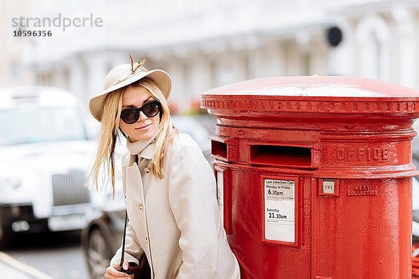 Stilvolle junge Frau wartet am roten Briefkasten  London  England  UK