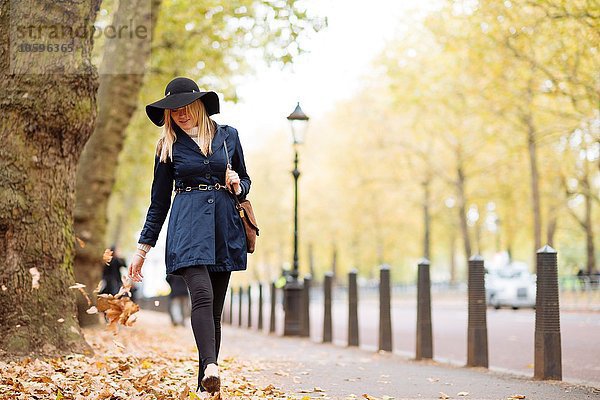 Stilvolle junge Frau beim Spaziergang durch das Herbstlaub im Stadtpark