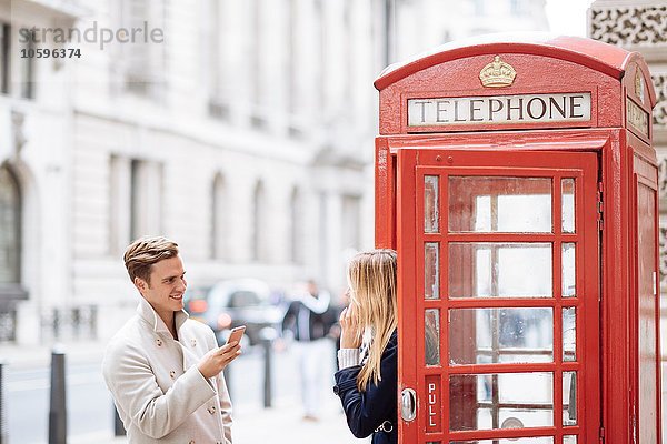 Junges Paar mit Smartphone neben roter Telefonzelle  London  England  UK