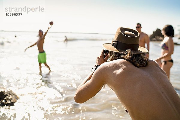 Junger Mann fotografiert Freunde beim American Football im Meer in Newport Beach  Kalifornien  USA