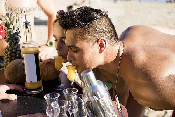 Junger Mann und Frau  die sich nach vorne lehnen  um einen Cocktail am Newport Beach  Kalifornien  USA zu trinken.
