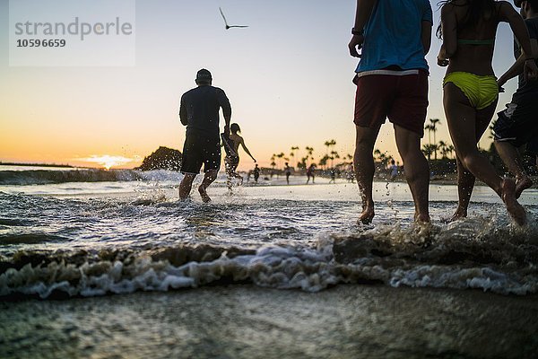 Rückansicht von erwachsenen Freunden  die bei Sonnenuntergang im Meer laufen  Newport Beach  Kalifornien  USA