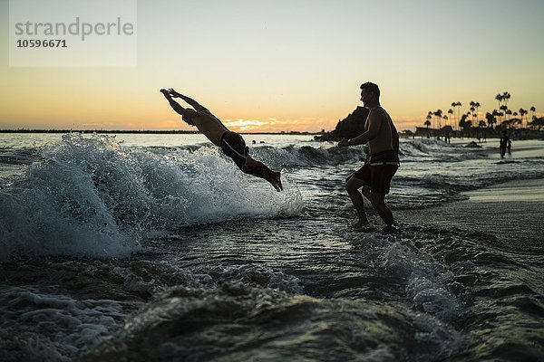 Junge Männer tauchen bei Sonnenuntergang ins Meer  Newport Beach  Kalifornien  USA