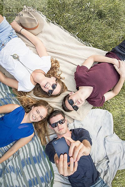 Gruppe junger Erwachsener auf Picknickdecken liegend  Selbstporträt mit dem Smartphone aufnehmend
