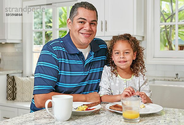 Vater und Tochter Seite an Seite an der Küchentheke beim Frühstücken  Blick auf die Kamera lächelnd