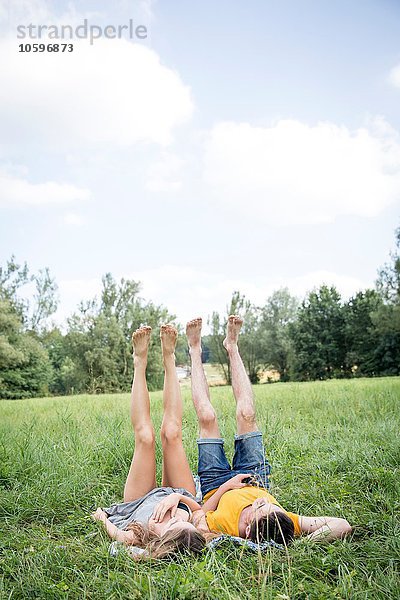 Junges Paar auf Gras im Feld liegend  Beine hochgezogen