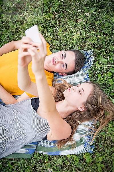 Junges Paar  das auf Gras auf dem Feld liegt und sich mit dem Smartphone selbst porträtiert.