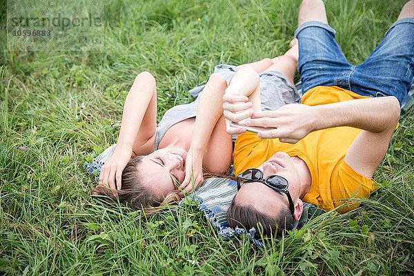Junges Paar auf Rasen im Feld liegend  mit Blick auf Smartphone