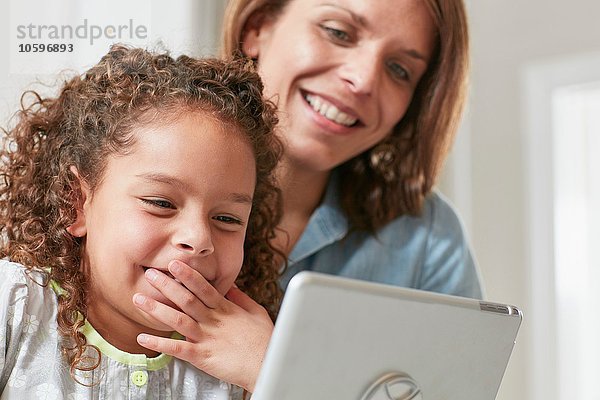 Niederwinkelansicht von Mutter und Tochter mit digitalem Tablett  Hand über den Mund lächelnd
