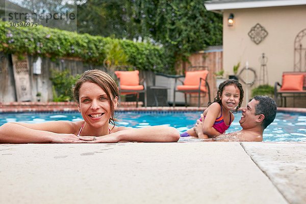Kopf und Schultern einer erwachsenen Frau mit Familie im Pool  die lächelnd auf die Kamera blickt.