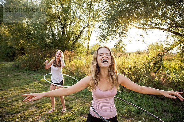 Zwei junge Mädchen in ländlicher Umgebung  die mit Hula-Reifen herumalbern