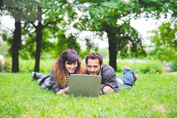 Vorderansicht eines jungen Paares  das auf dem Rasen liegt und lächelt.