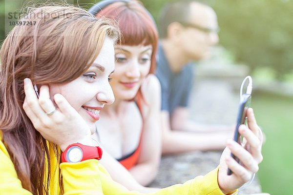 Junge Frauen  die ein Smartphone benutzen  lehnen sich an eine niedrige Wand.